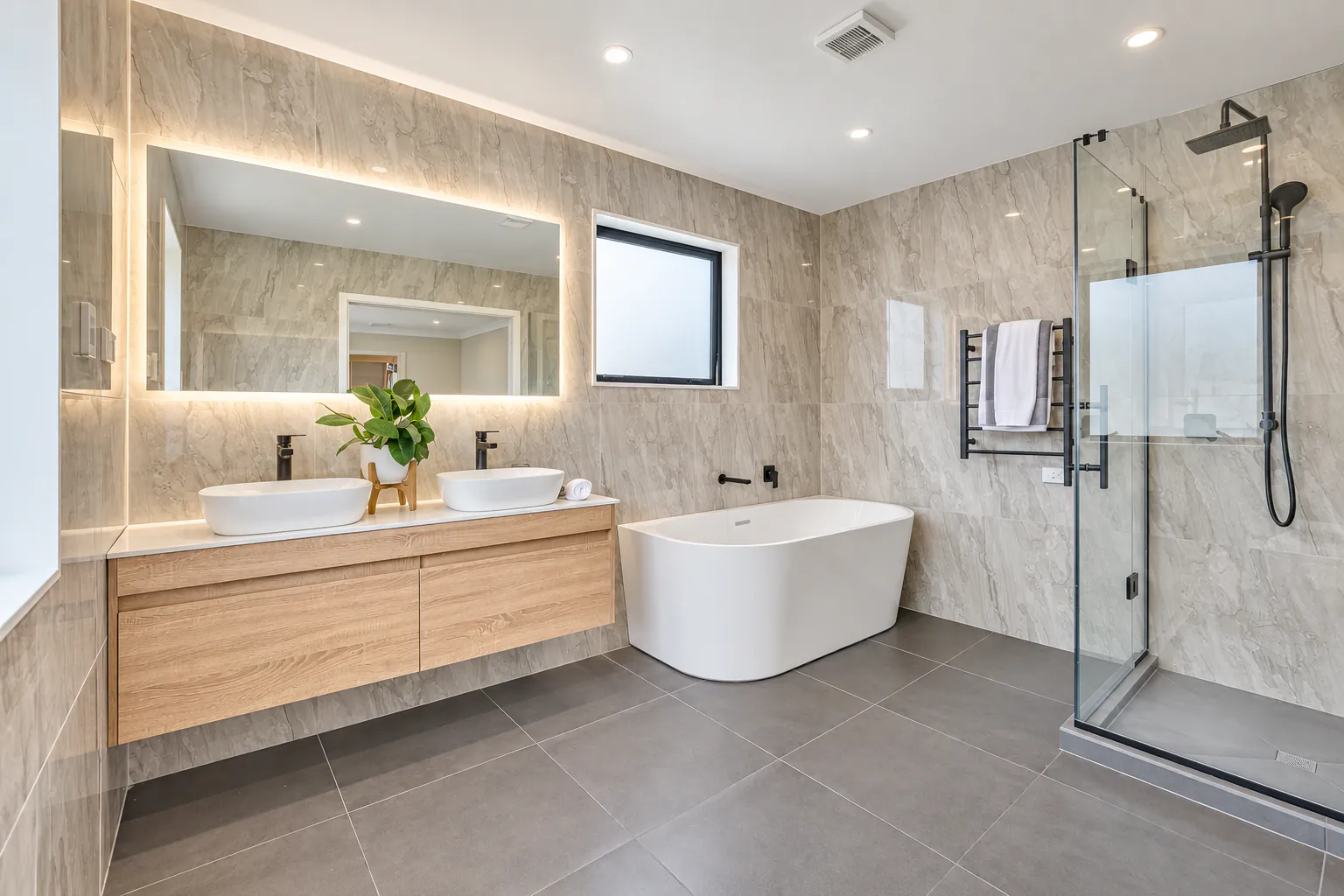 AI-retouched project photograph: the main bathroom with a timber double vanity, freestanding bath and glazed shower at Bucklands Beach 26.