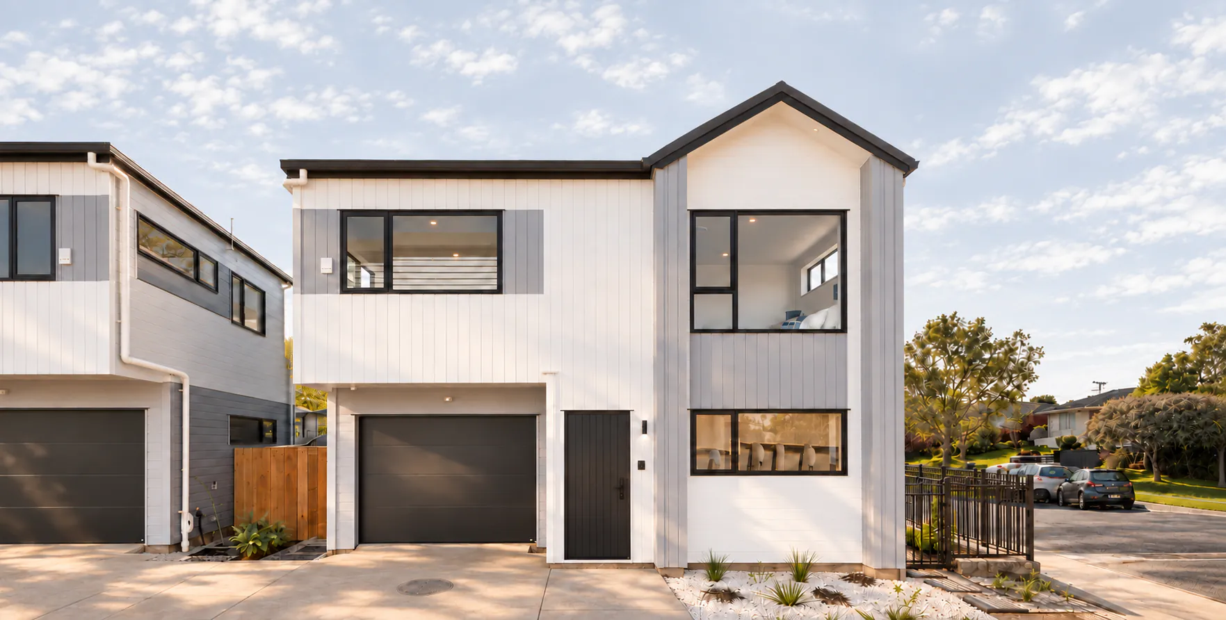 AI-retouched project photograph: white and grey two-storey homes at Botany Downs, viewed from the driveway.